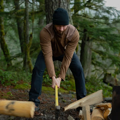 Man splitting firewood outdoors in rugged GORUCK apparel in a forest setting