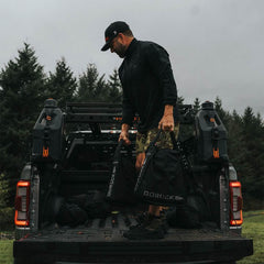 Man loading GORUCK sandbags and gear onto truck bed outdoors, featuring rugged rucking equipment.