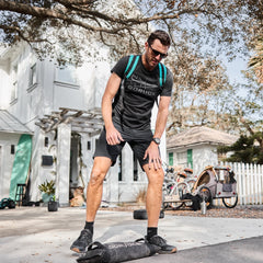 A man in athletic wear stands outside on a driveway, stepping onto the Simple Training Sandbags for a workout, with bikes and trees visible in the background.