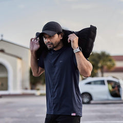 Man wearing GORUCK black hat and shirt lifting rucking sandbag outdoors in parking lot