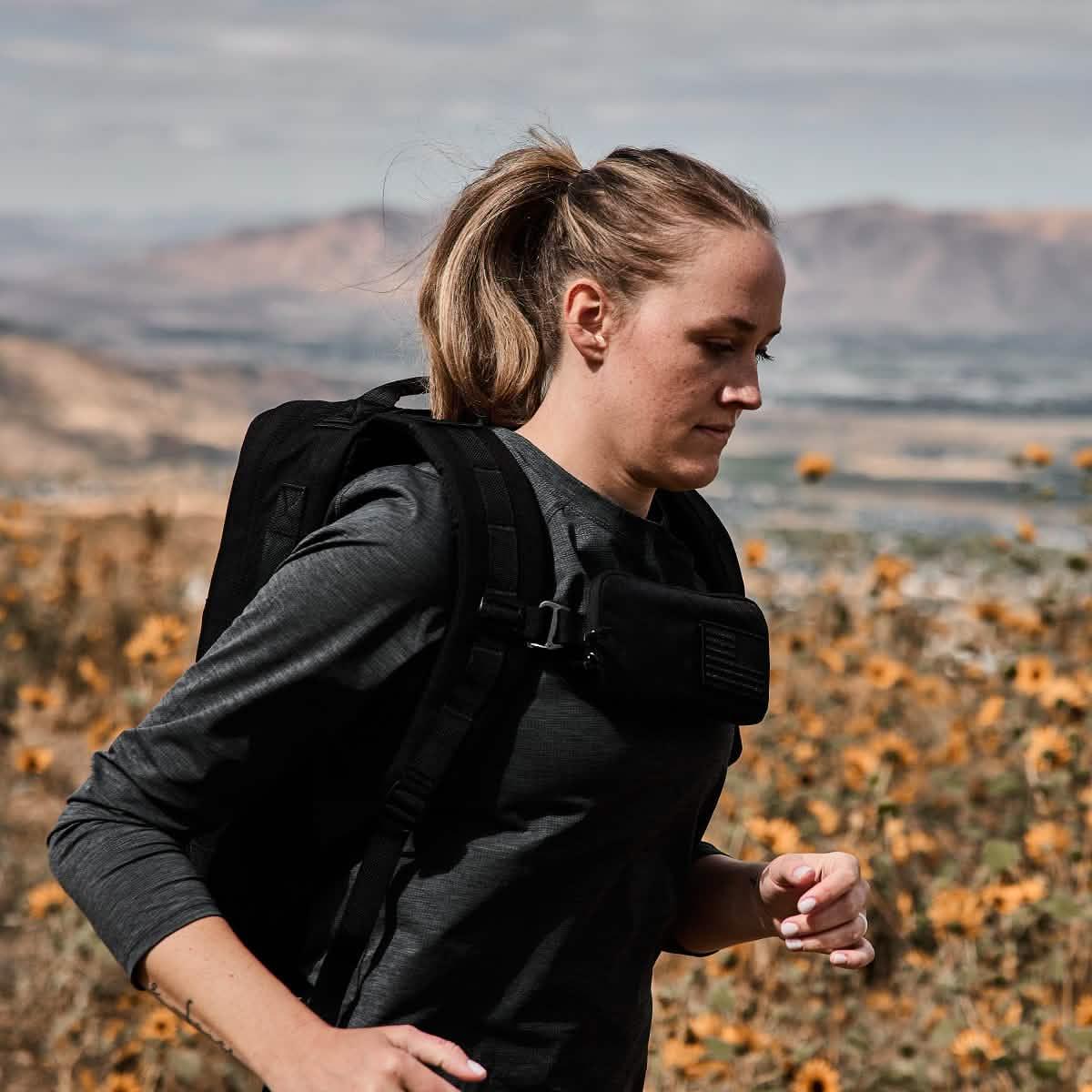 Woman rucking outdoors wearing GORUCK backpack and sternum pouch in a field of flowers.