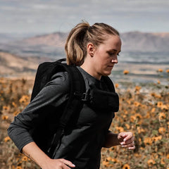 Woman rucking outdoors wearing GORUCK backpack and sternum pouch in a field of flowers.