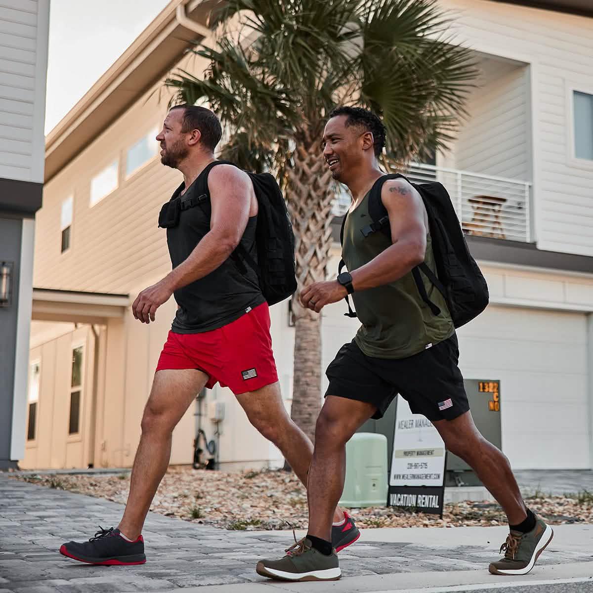 Two men rucking with GORUCK gear and backpacks outside modern homes on a sunny day