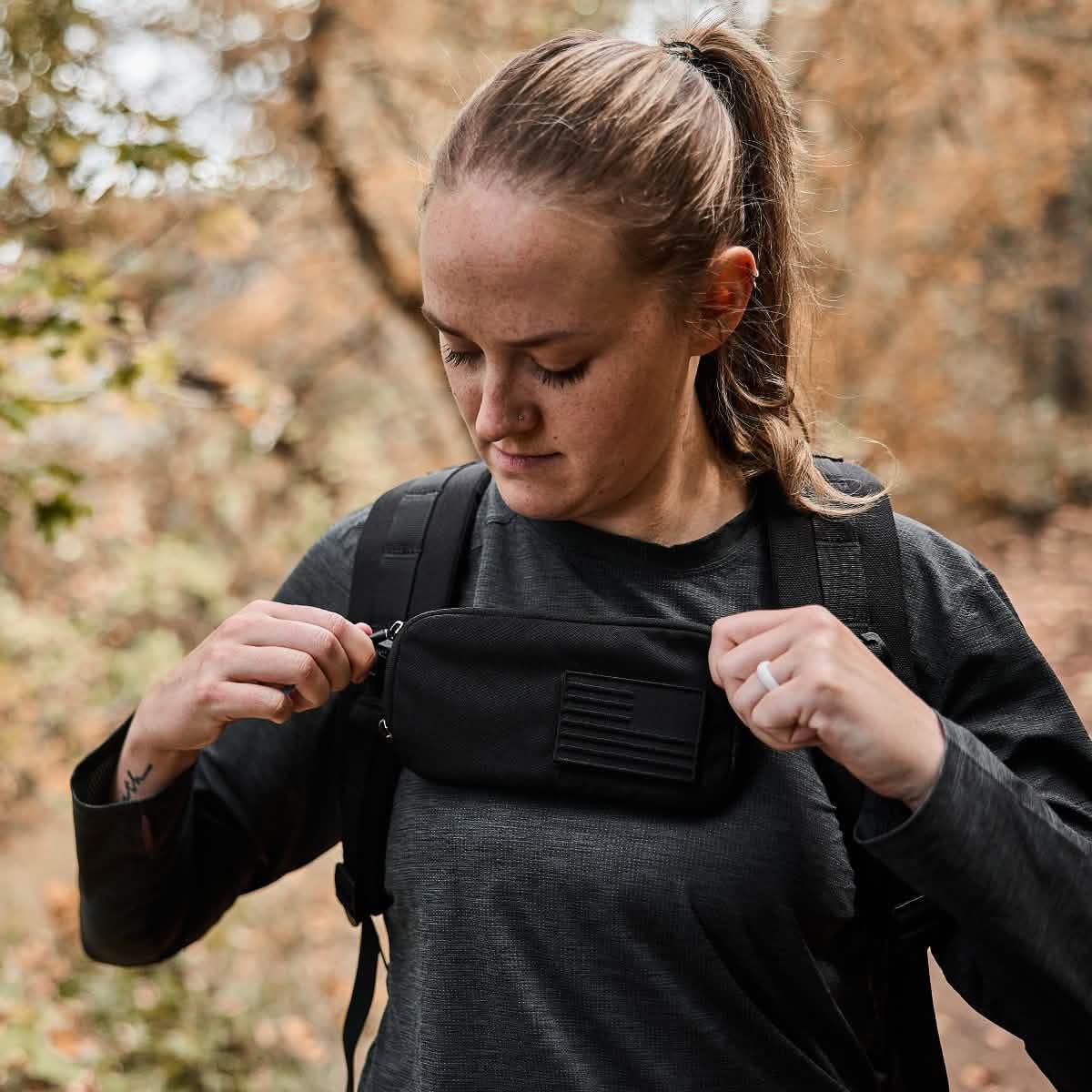 Woman outdoors adjusting GORUCK sternum pouch on rucksack strap, autumn background