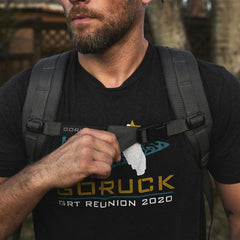 Man adjusting GORUCK sternum strap on grey rucksack outdoors, wearing GORUCK t-shirt
