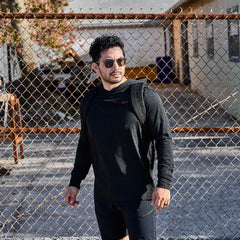 Man wearing GORUCK black hoodie and rucksack outdoors near chain-link fence