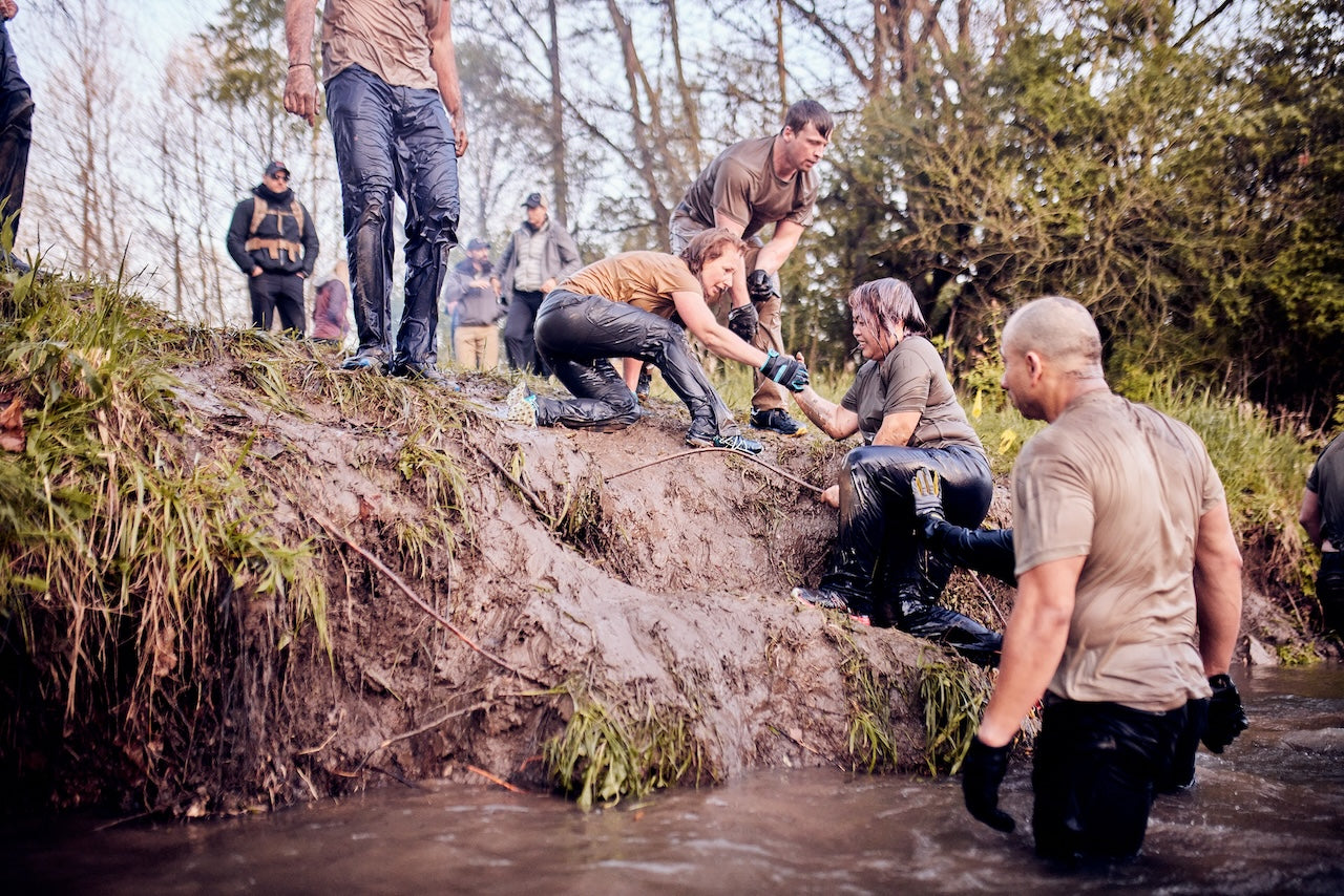 People help each other climb up a muddy riverbank during an outdoor teamwork challenge.