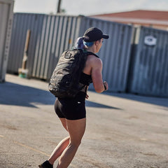 Woman rucking outdoors wearing GORUCK backpack and athletic gear near shipping containers
