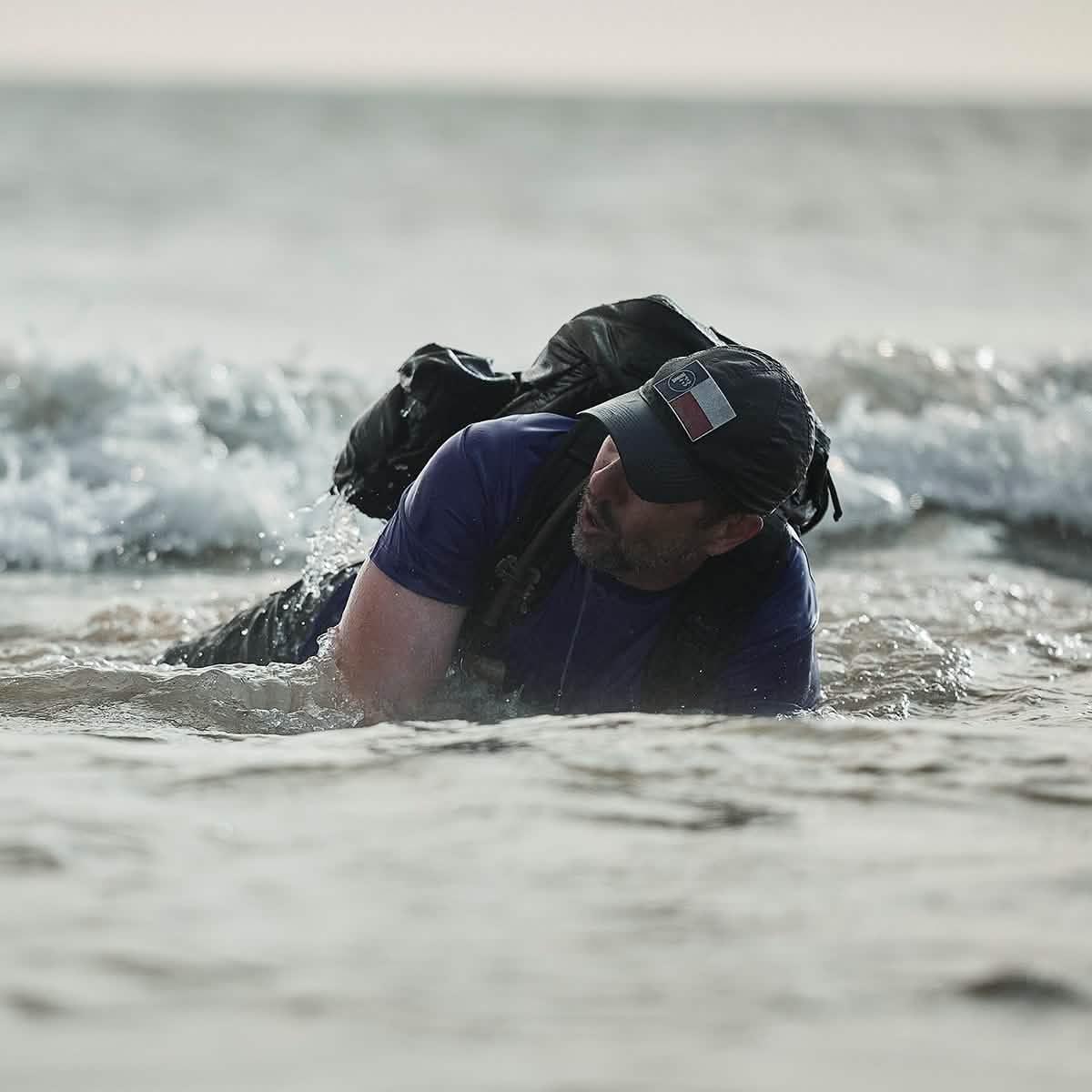 Man wearing GORUCK backpack crawling through ocean surf, showcasing tough rucking gear
