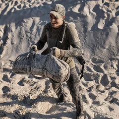Man rucking with a sandbag on sandy terrain wearing GORUCK gear and cap