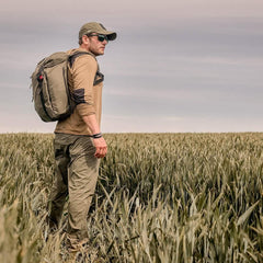 Man rucking with GORUCK gear and olive backpack in a grassy field under cloudy sky