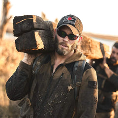 Man wearing GORUCK cap and sunglasses carrying heavy log outdoors during rucking event