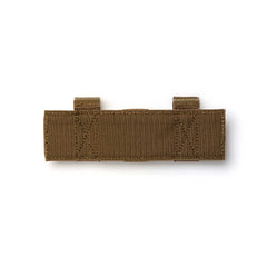 The Tourniquet Attachment is a brown tactical fabric strap with two loops and reinforced stitching for secure tourniquet storage, shown laid flat on a white background.