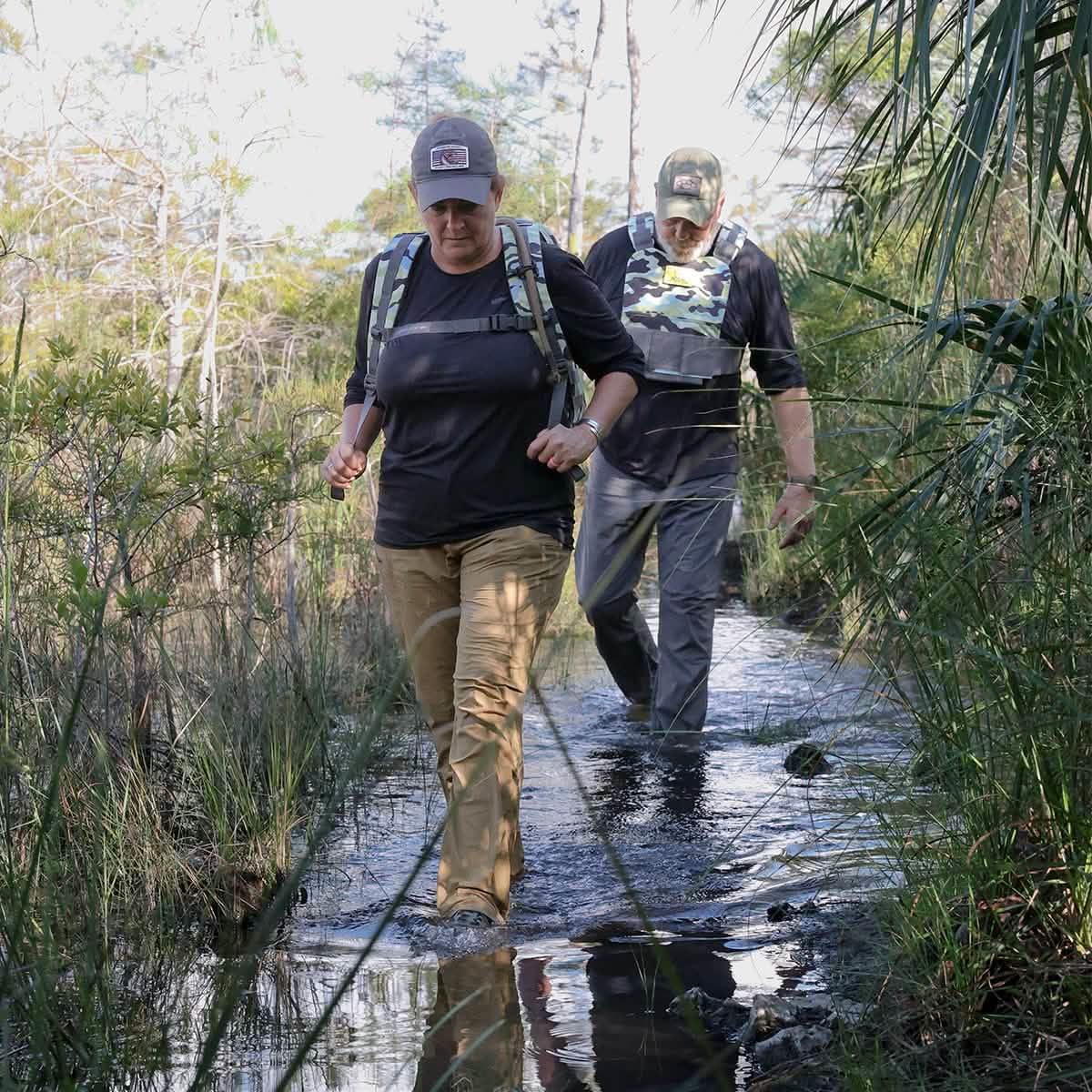 Two people rucking in GORUCK gear, trekking through a muddy forest trail.