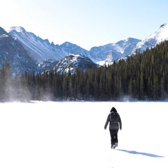 Person rucking in snow near pine forest and mountains, wearing GORUCK gear, winter landscape