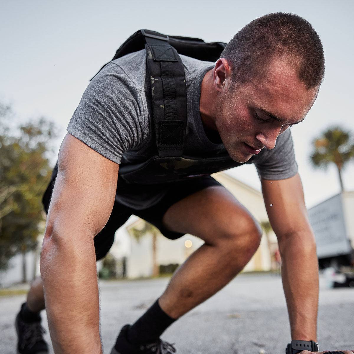 A man in workout gear leans forward, sweating and exhausted, during outdoor exercise while wearing the Training Weight Vest 2.0.