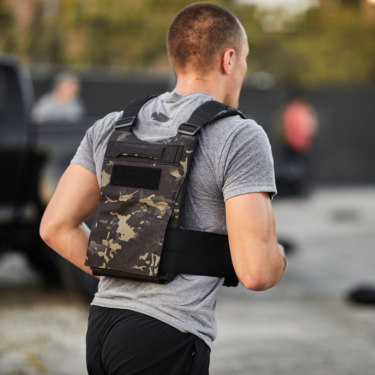 A man runs outdoors wearing a gray t-shirt and the Training Weight Vest 2.0, loaded with ruck plates.
