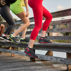 Women wearing GORUCK Ballistic Trainers in wolf grey and red, exercising outdoors on wooden steps