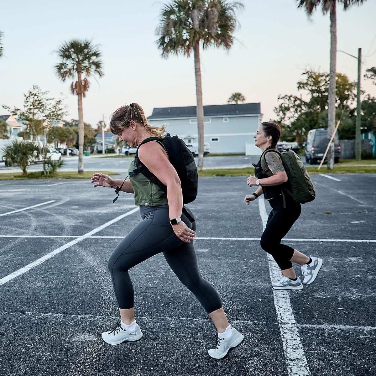 Two women rucking in GORUCK ballistic trainers with backpacks in a parking lot
