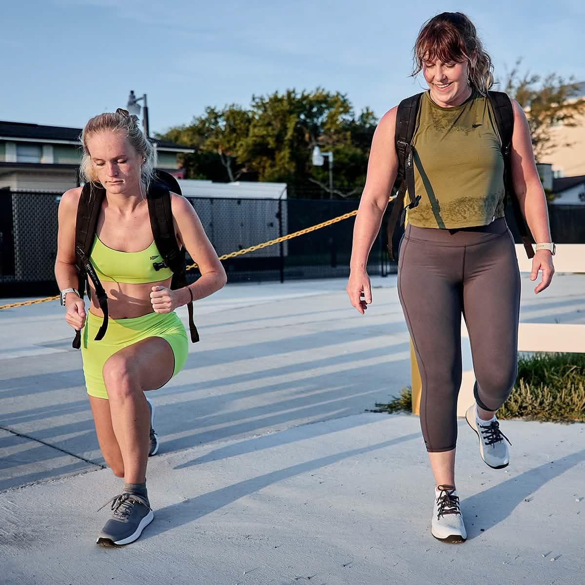 Two women outdoors in GORUCK gear, wearing rucksacks and athletic trainers, exercising together