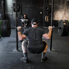 Man performing barbell squat in gym with black GORUCK rucking gear and weight plates