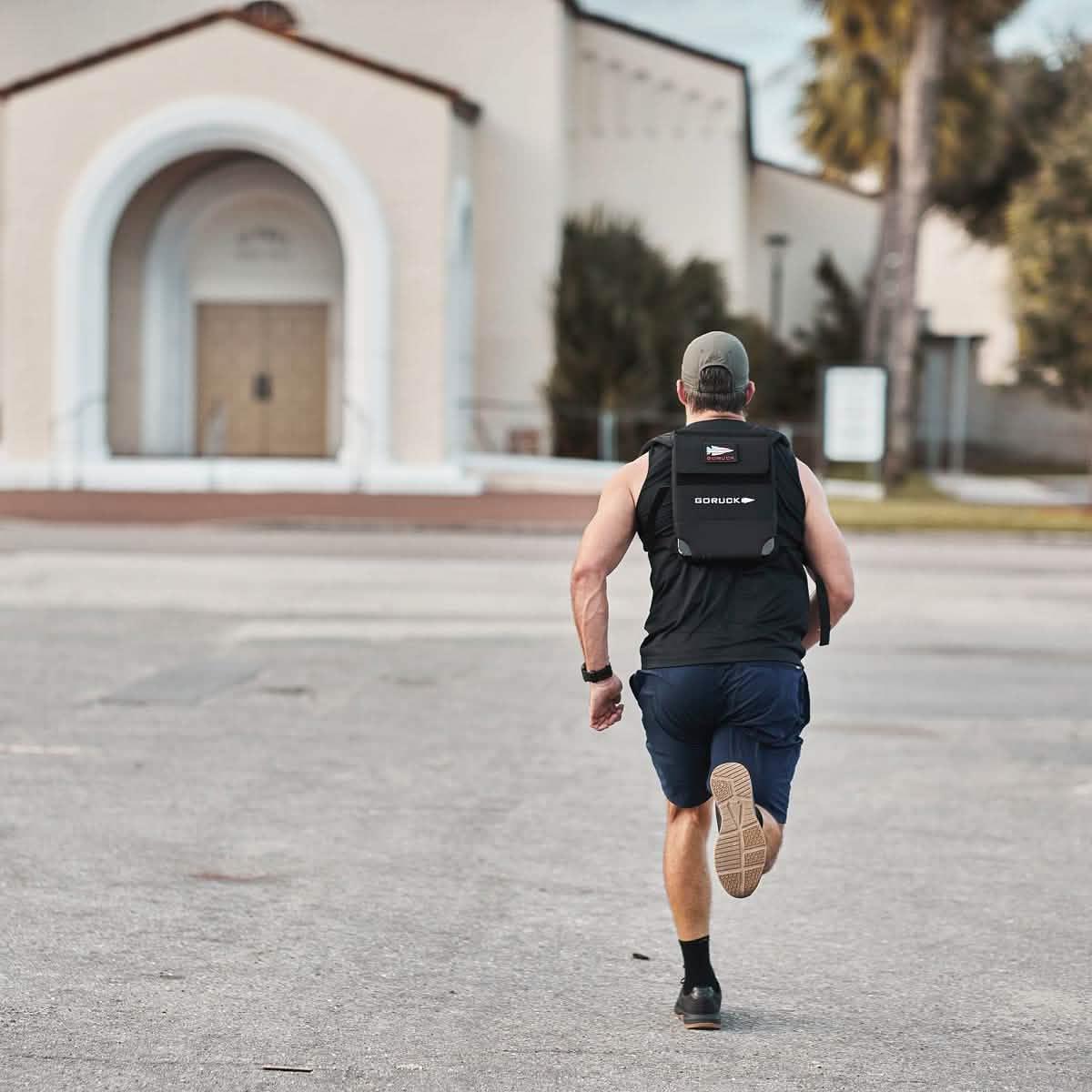 Man running outdoors wearing GORUCK rucksack, black athletic gear, and a cap