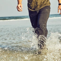 Man wearing GORUCK black pants walking through ocean waves, rugged outdoor apparel