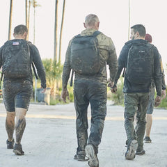 Group of people in muddy clothes wearing GORUCK backpacks during outdoor rucking event