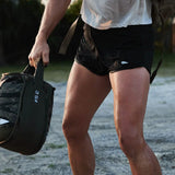 A person outdoors holds a gym bag, wearing black Training Shorts that feature ToughStretch fabric, with their torso and legs visible.