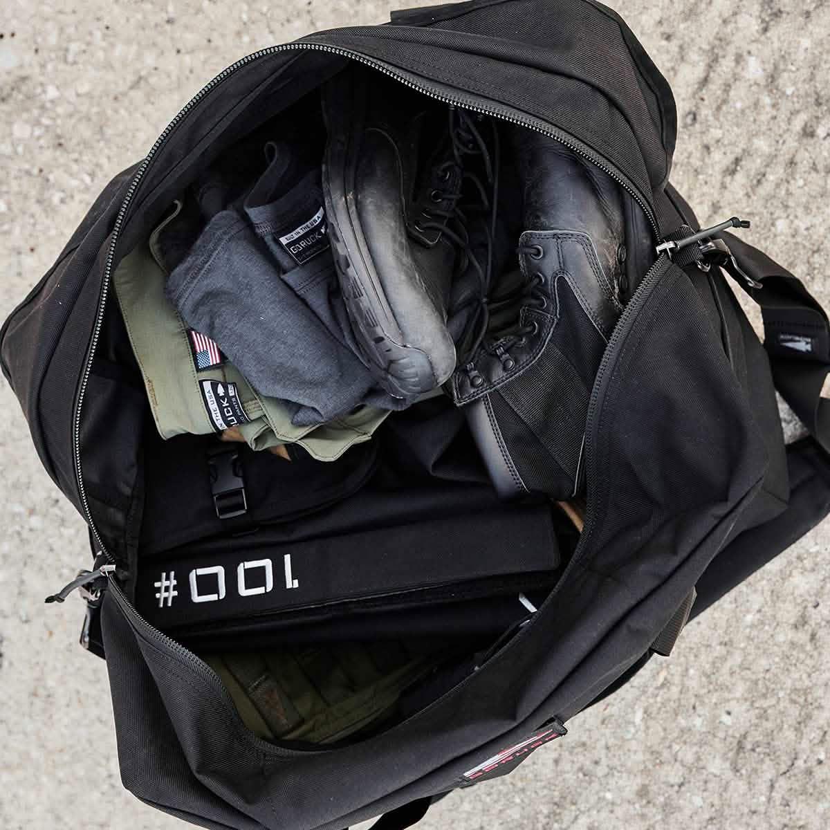 GORUCK rucking gear in open black duffel, including boots, apparel, and weight plate