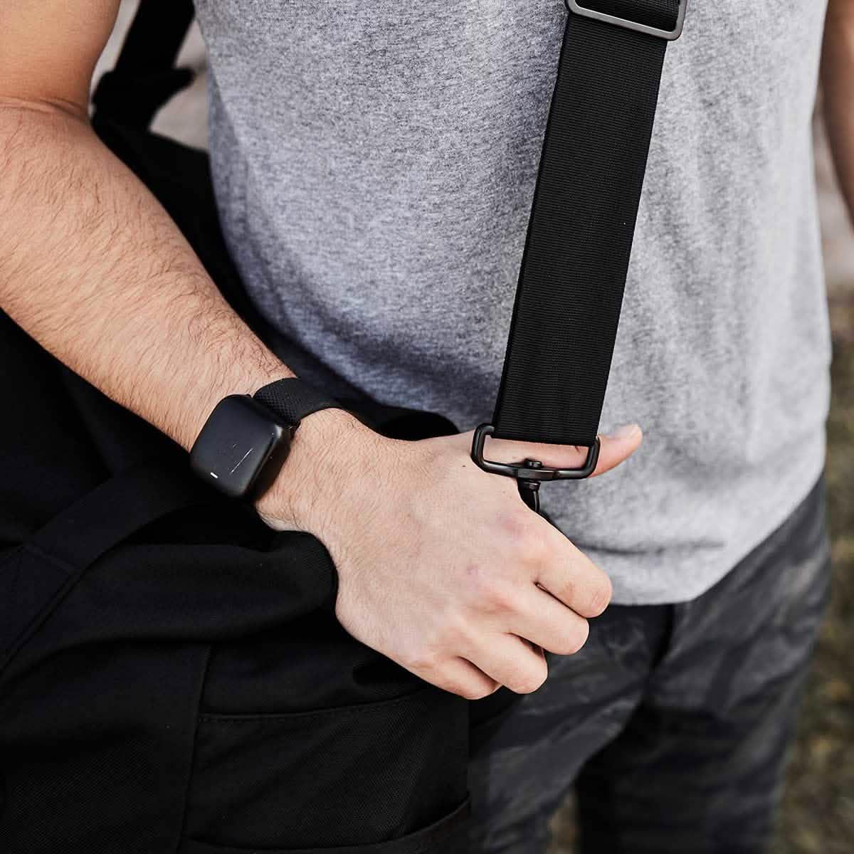 Man in grey shirt holding GORUCK rucking gear bag with sturdy black strap outdoors