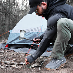 Man setting up a tent outdoors with axe, wearing GORUCK outdoor gear and rucking shoes