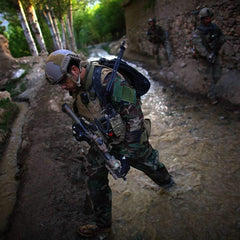 Rucking gear in action: soldier in tactical gear crossing stream, forested path, GORUCK