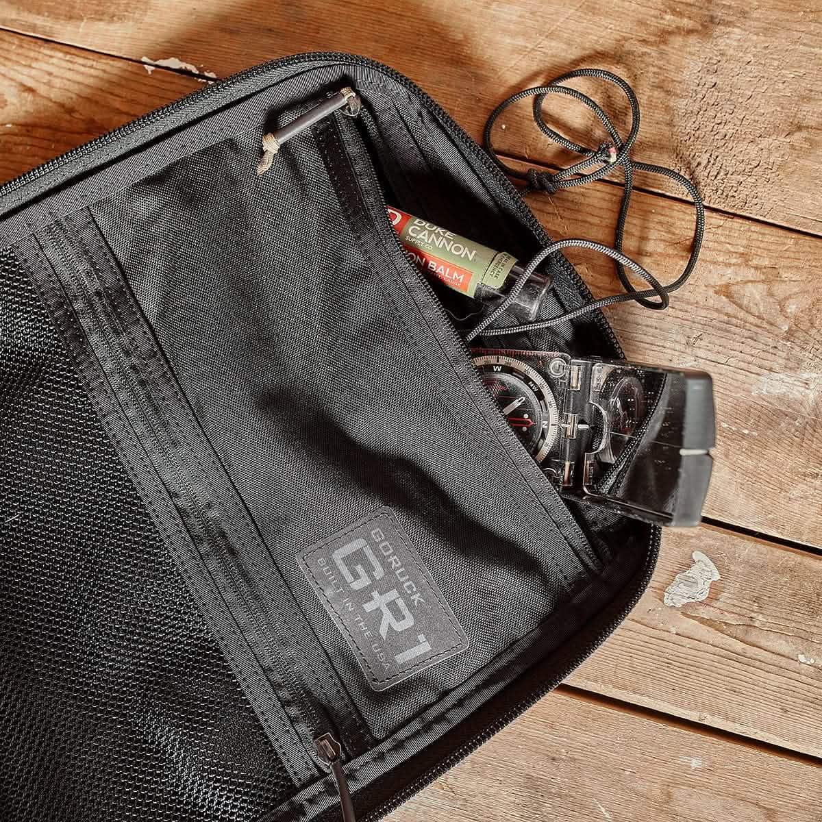 GORUCK GR1 rucksack interior with compass, lip balm, and cord on a wooden surface