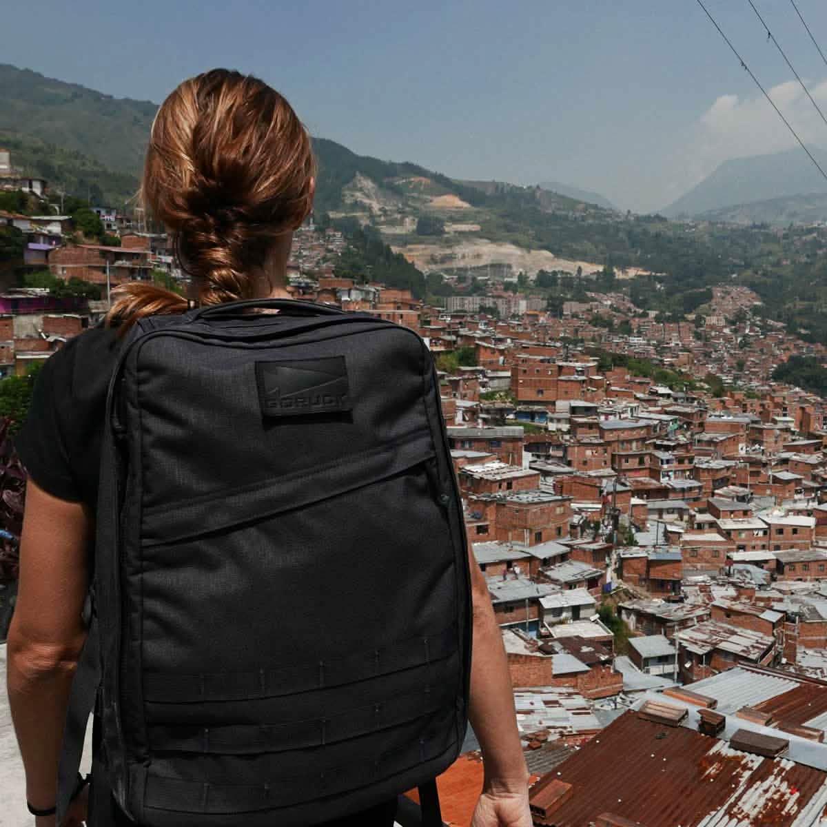Woman with GORUCK backpack overlooking cityscape and mountains, outdoor travel scene