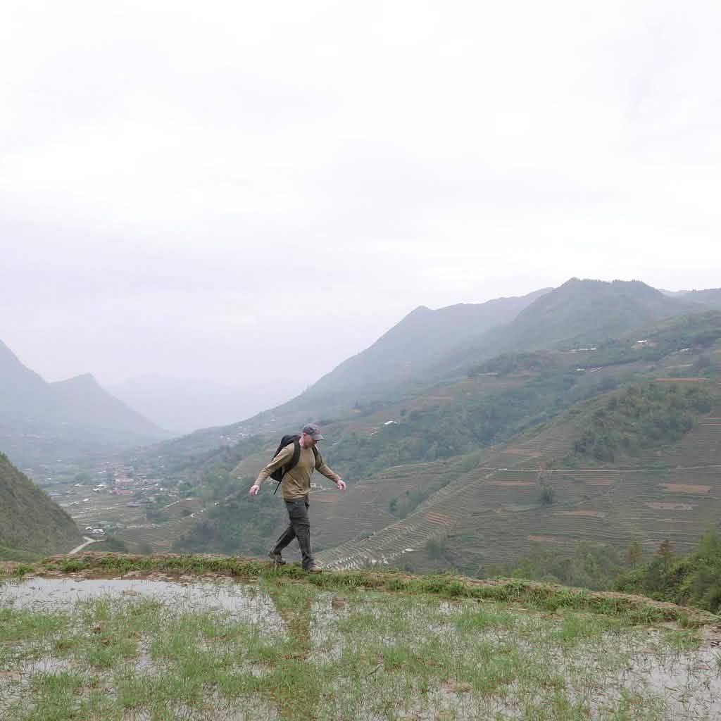 Man rucking with GORUCK backpack on a misty mountain trail in Vietnam overlooking terraced hills.