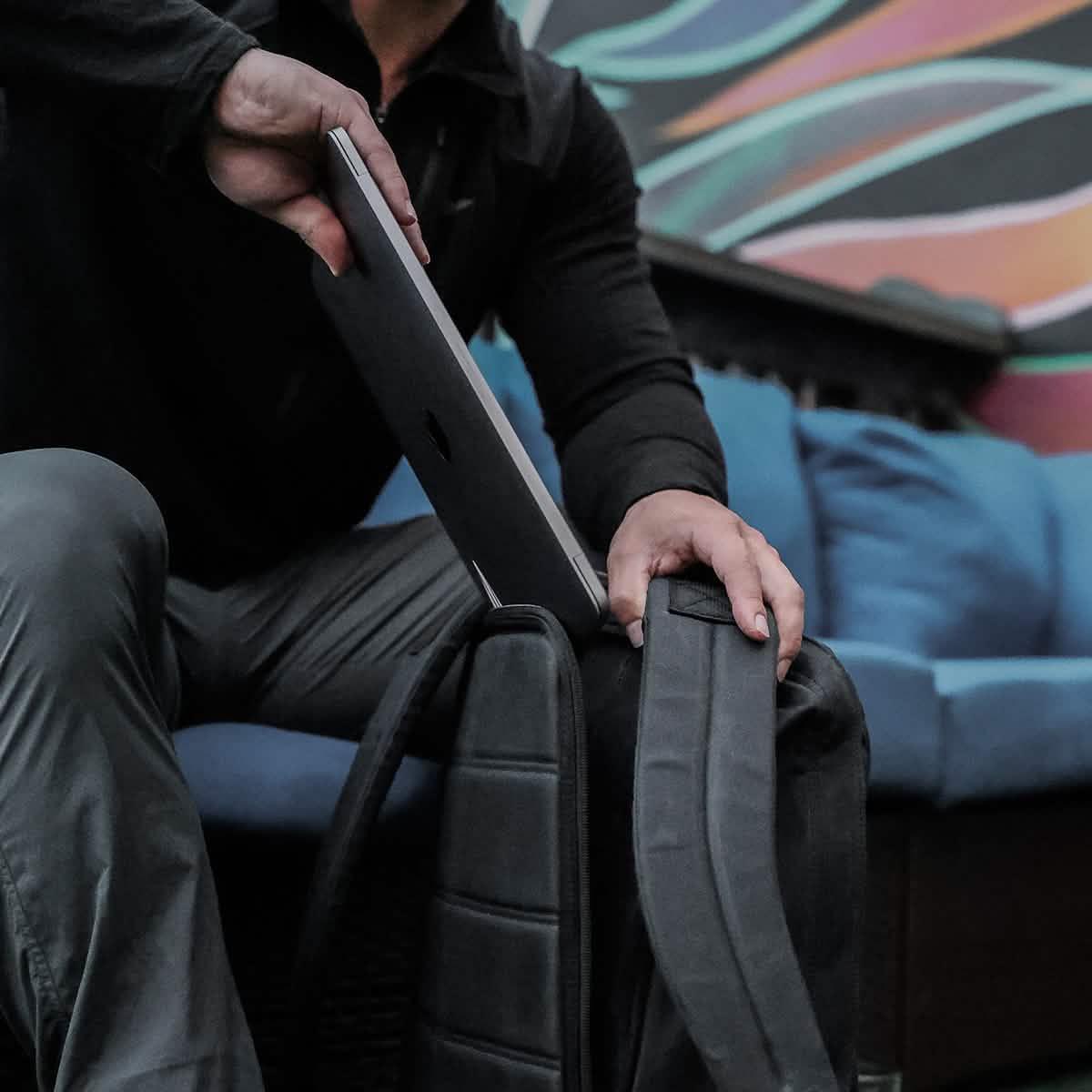Person placing laptop into GORUCK rucksack on blue couch with colorful mural background