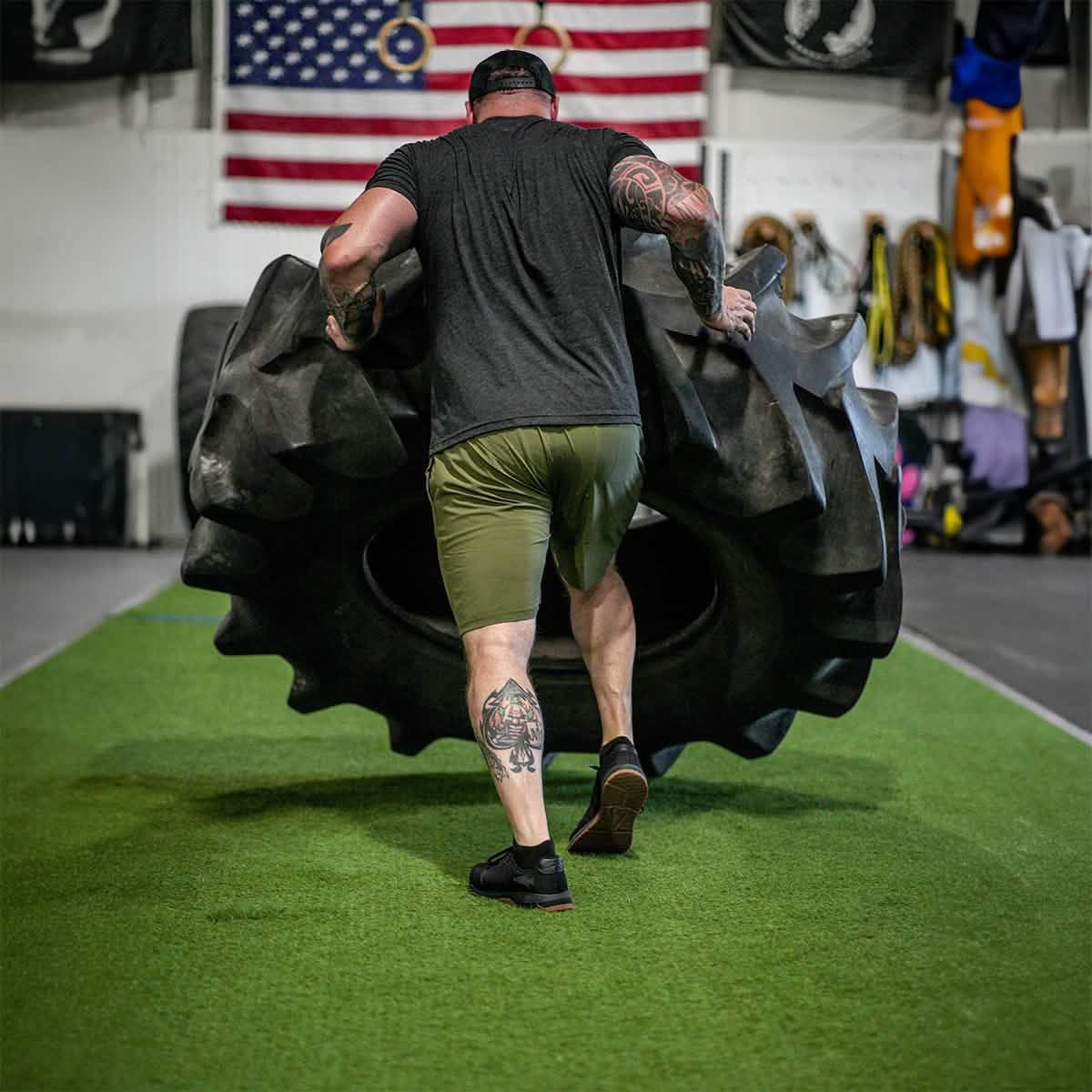 Man flipping large tire in gym with American flag, showcasing GORUCK rucking strength training