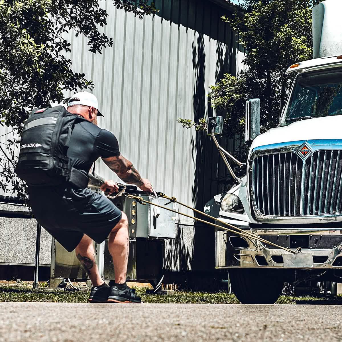 Man wearing GORUCK rucksack pulling a large truck outdoors for strength training