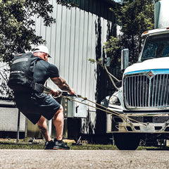 Man wearing GORUCK rucksack pulling a large truck outdoors for strength training