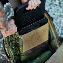 Person placing a GORUCK weight plate into a camo rucking backpack outdoors