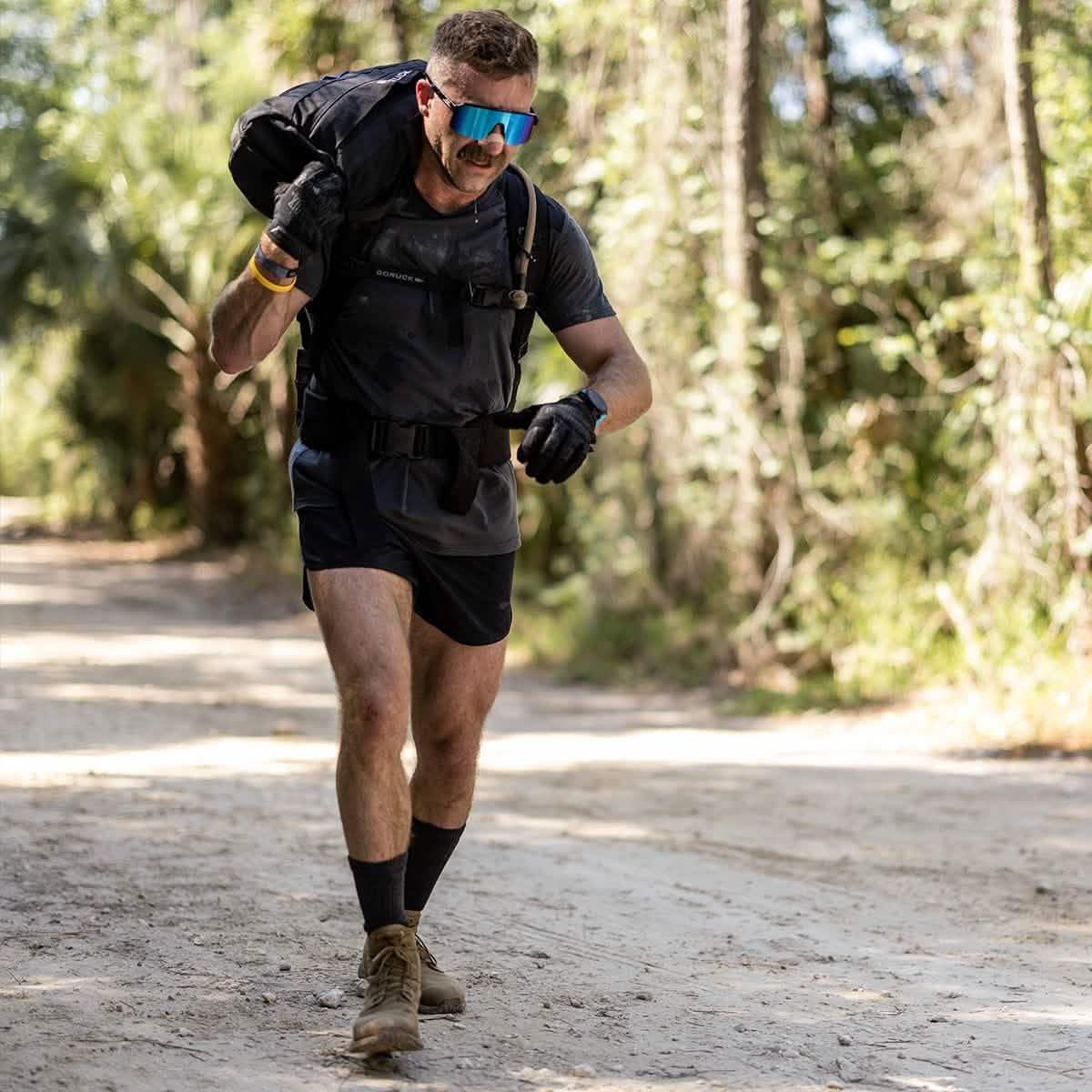 Man rucking with GORUCK backpack on trail, wearing training gear and sunglasses outdoors