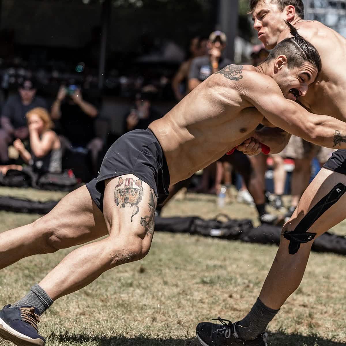 Two athletic men wrestling outdoors at a GORUCK event, showing intense physical competition.