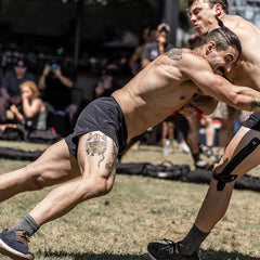 Two athletic men wrestling outdoors at a GORUCK event, showing intense physical competition.