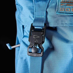 Close-up of the GORUCK M23 rucksack in Tidal Blue with Speed Tan accents, featuring a black buckle fastener and a short strap. The textured fabric resembles that of an M1945 field pack, with part of the orange logo visible on the upper right corner of the 21L backpack.