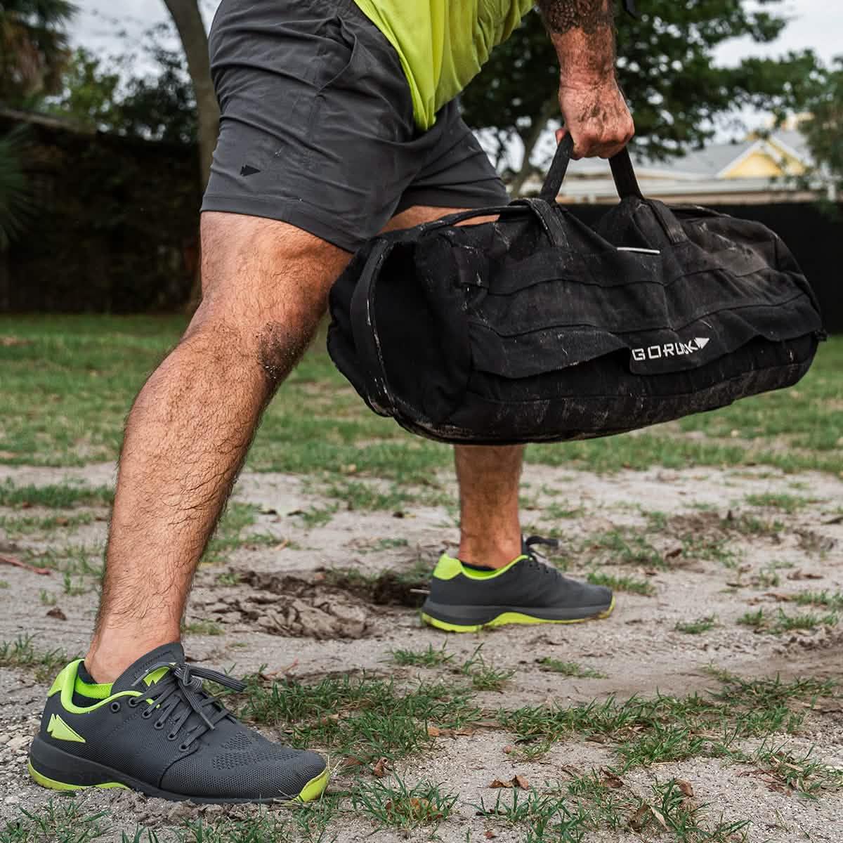 Man outdoors lifting GORUCK ruck bag, wearing athletic gear and GORUCK sneakers