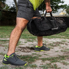 Man outdoors lifting GORUCK ruck bag, wearing athletic gear and GORUCK sneakers