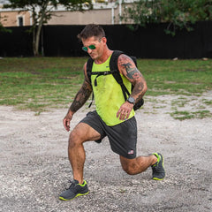 Man in neon tank top and backpack doing outdoor lunge, GORUCK rucking workout gear