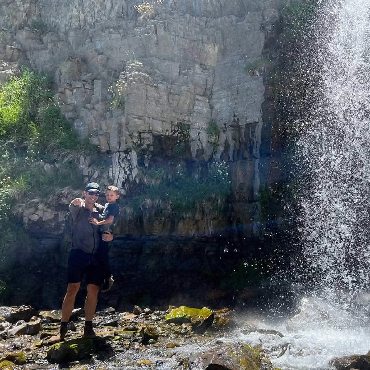 Man and child by a waterfall in outdoor gear, rugged rocky backdrop, GORUCK adventure
