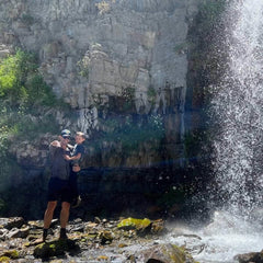 Man and child by a waterfall in outdoor gear, rugged rocky backdrop, GORUCK adventure